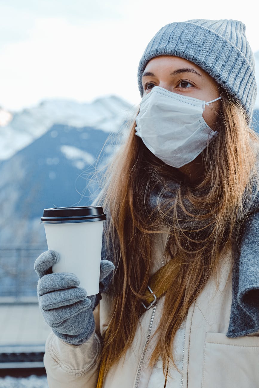 woman wearing face mask holding white disposable cup